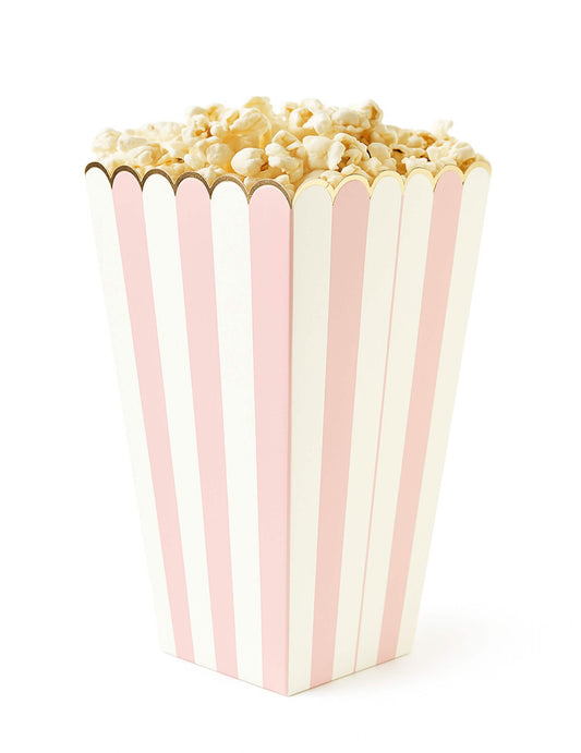 Zoom sur une boîte remplie du boîtes à pop corn à rayures pour fête rose pastel et blanc avec bordure dorée