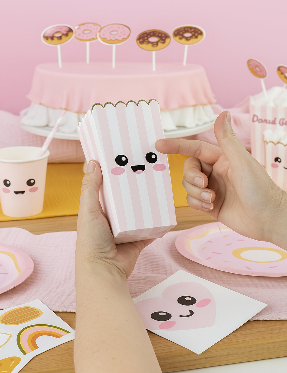 Détail du sticker visage sur les boîtes à pop corn à rayures pour fête rose pastel et blanc avec bordure dorée