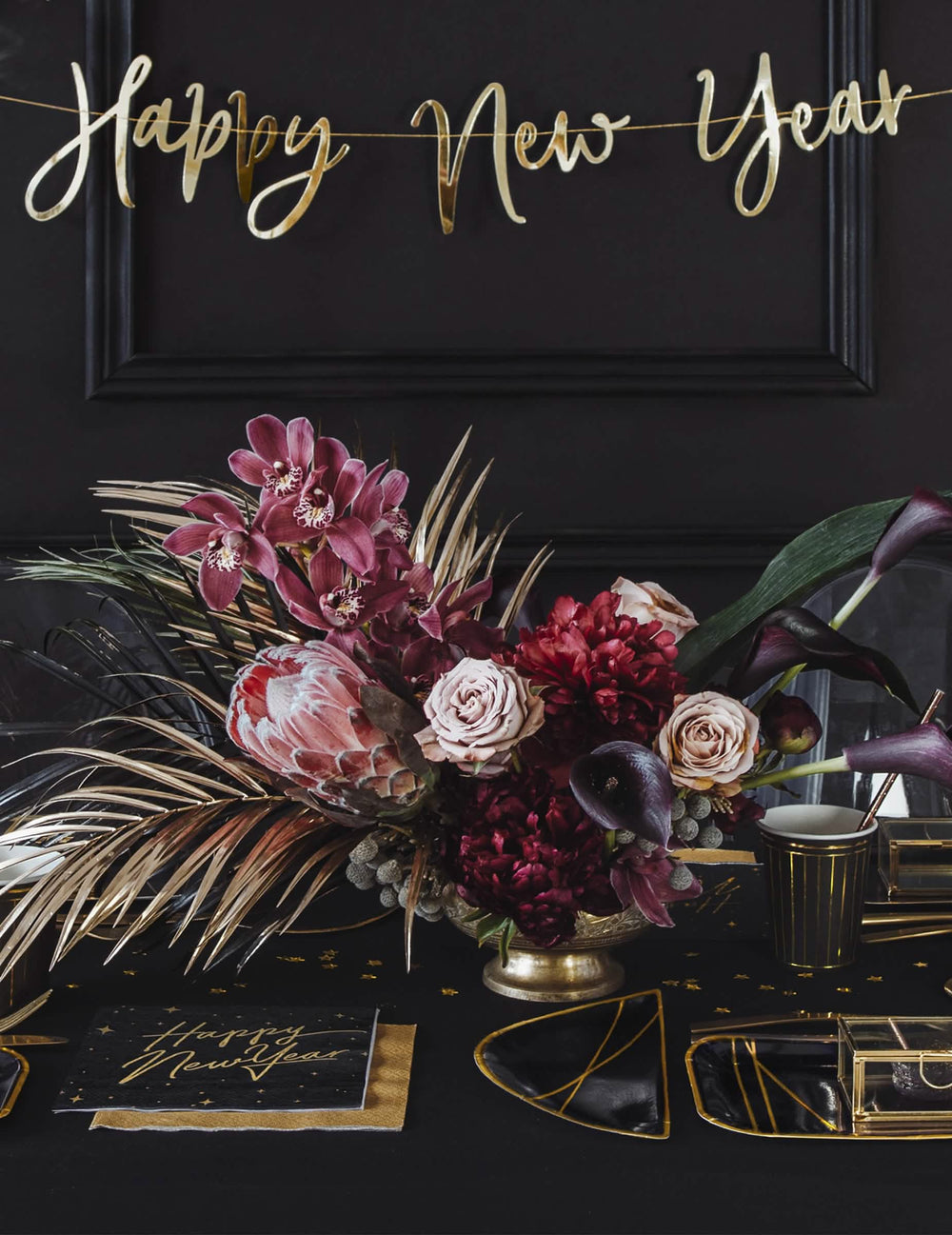 Postavitev na praznično mizo z črnimi in zlatimi papirnatimi prtički Happy New Year z zvezdastim okrasjem