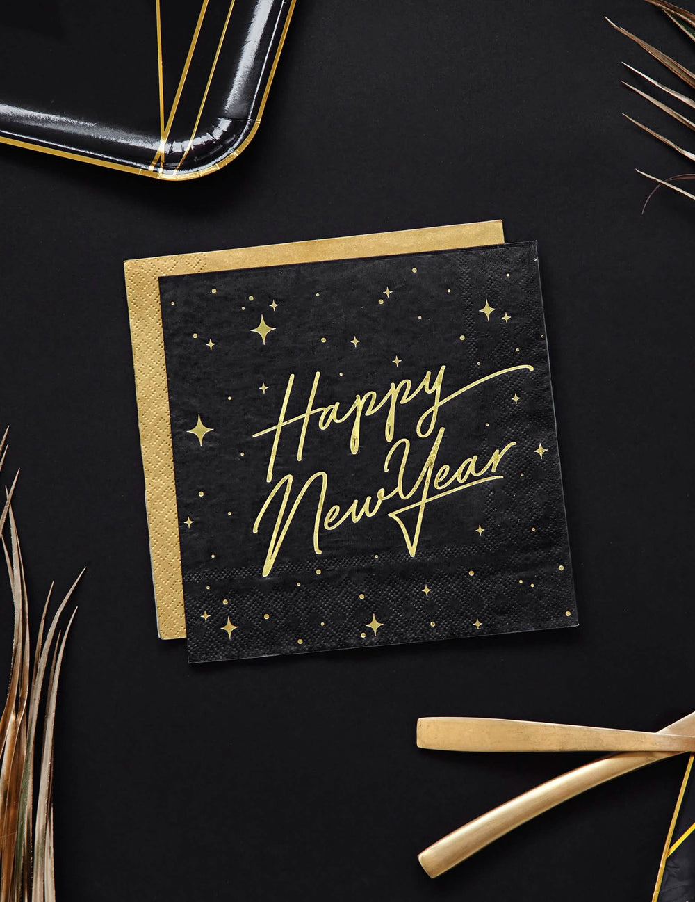 Pogled od zgoraj na črne in zlate papirnate prtičke Happy New Year z zvezdastim okrasom