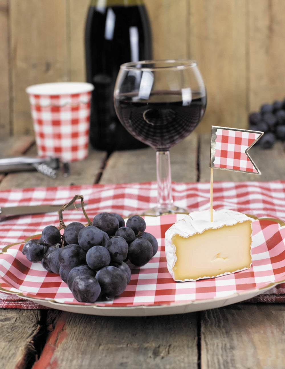 Mise en scène avec fromage et raisin du gobelet en carton festonné vichy pour fête rouge et blanc