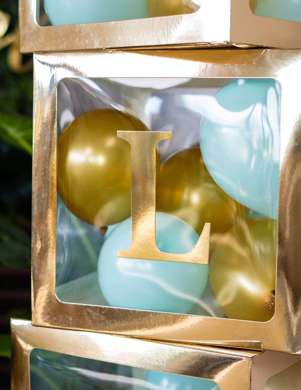 Gros plan sur la lettre L du cube à ballons transparent pour fête doré personnalisable